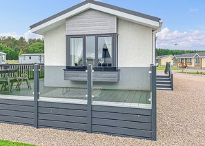 Een gelijkvloerse stacaravan met balkon, een grindpad en een heldere lucht.