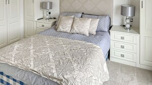 A bedroom with a bed, two bedside tables, a nightstand, a headboard, and a wall-mounted lamp.