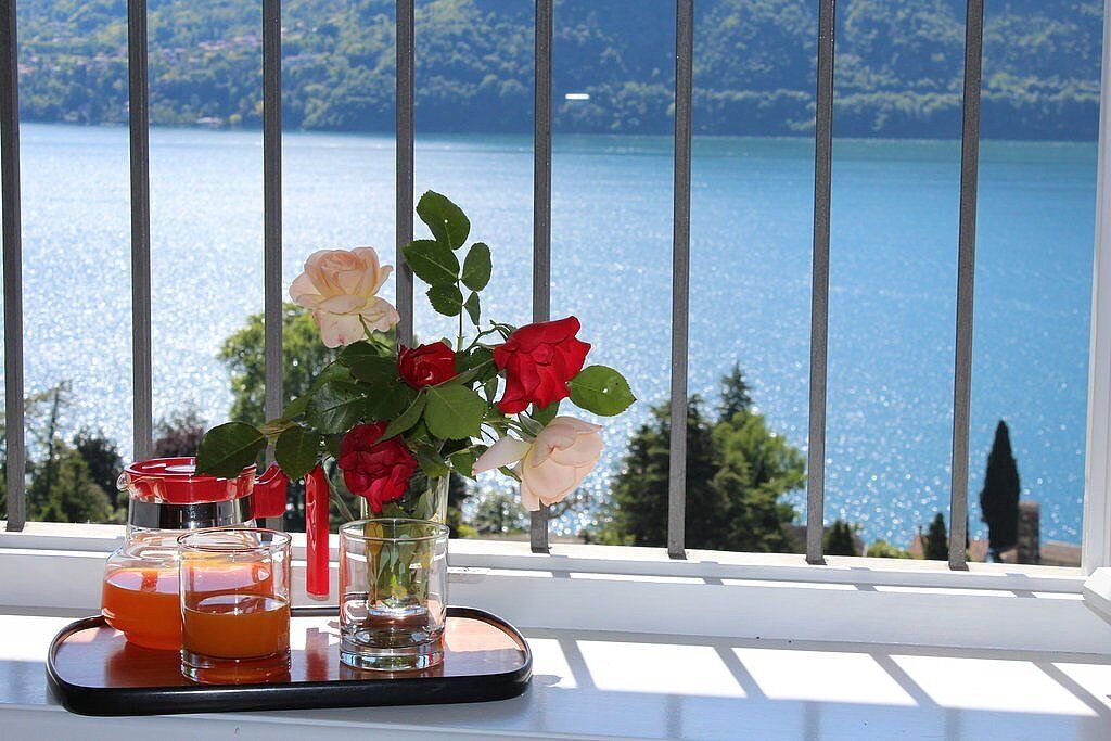 Ein Tablett mit Getränken und Blumen auf einem Balkon mit Blick auf einen See.