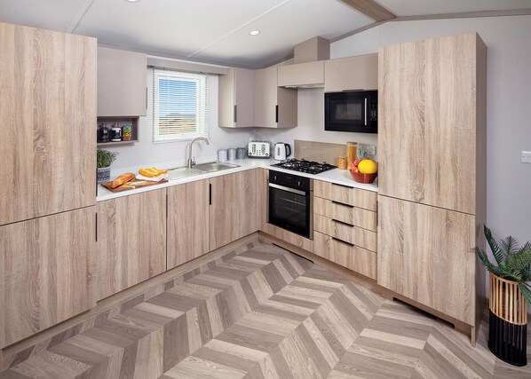 A modern kitchen with wooden cabinets, a microwave, a gas stove, and a herringbone-patterned floor. - A recent addition to the Searles Leisure Resort holiday hire fleet. (Hunstanton)