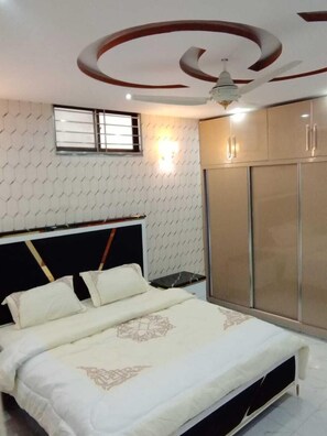 A bedroom with a bed, wardrobe, and ceiling fan. - Al Rehman Palace 1 (Lahore)