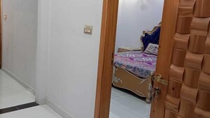 A room with a wooden door, white walls, and a bed with a patterned bedspread. - Al Rehman Palace 1 (Lahore)