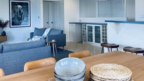 A modern living room with a sofa, a dining table with plates and glasses, and a kitchen area with a counter and cabinets.