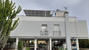 Ein modernes Gebäude mit flachem Dach, Solaranlagen und einer überdachten Außenbereich-Sitzgelegenheit.