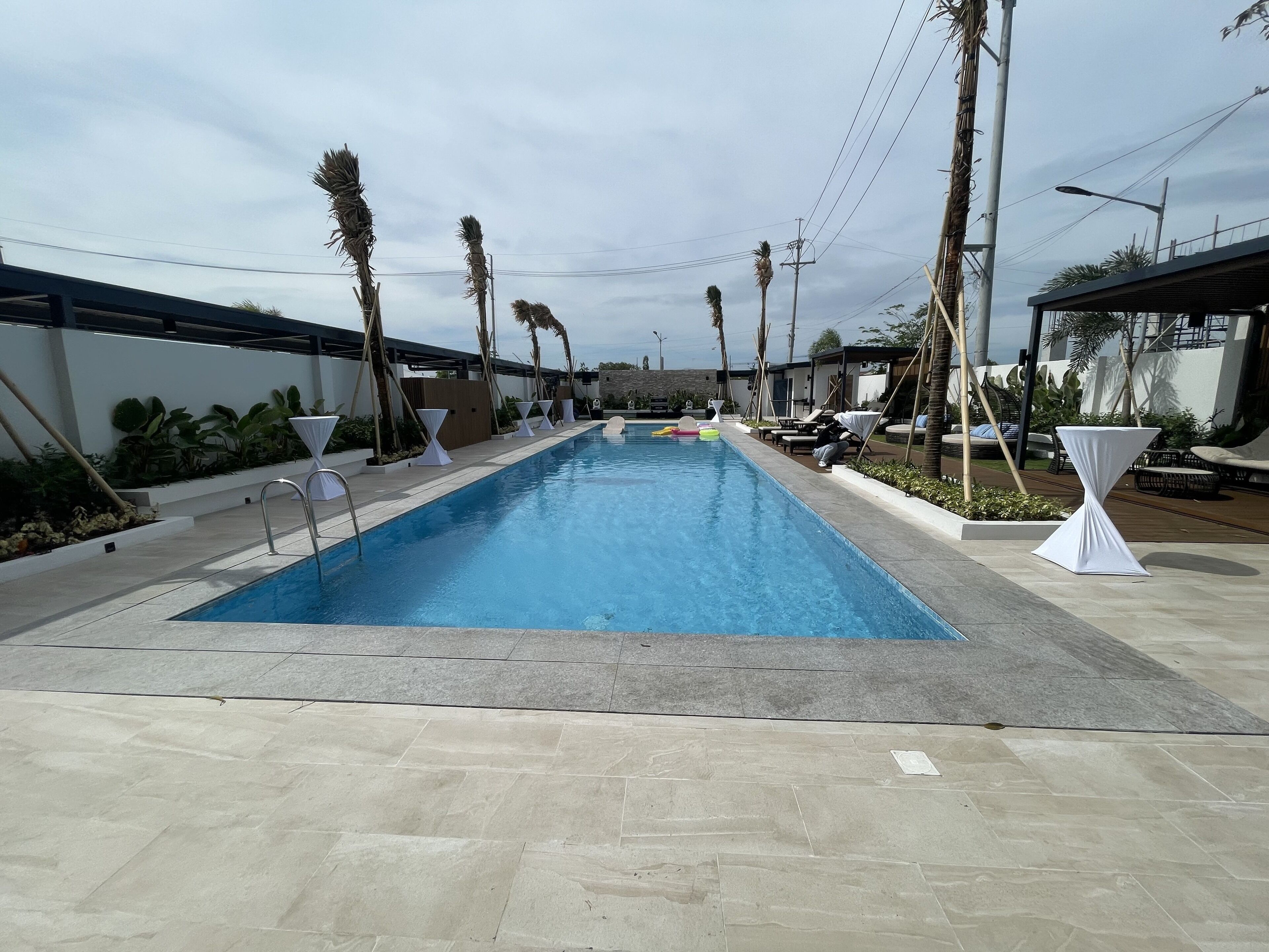 A rectangular swimming pool with a tiled deck, surrounded by palm trees and lounge chairs.