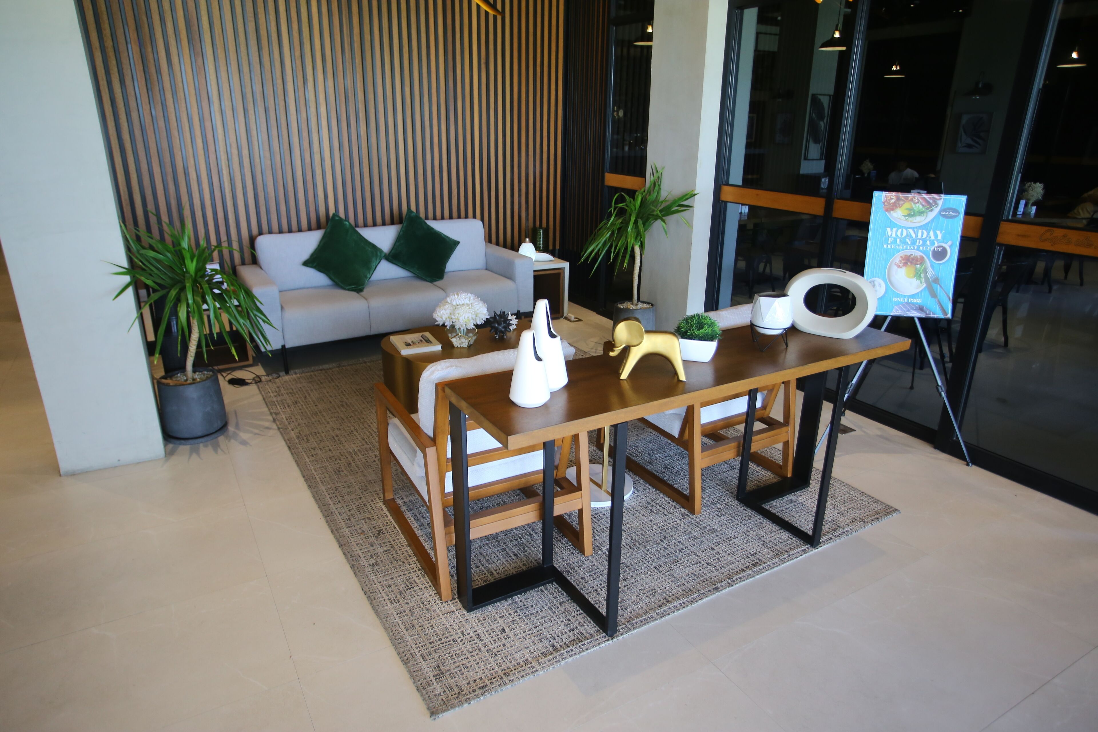 Un interior moderno con sofá, mesa de centro y mesa de comedor con sillas. Se ven plantas en macetas y un atril para el menú.
