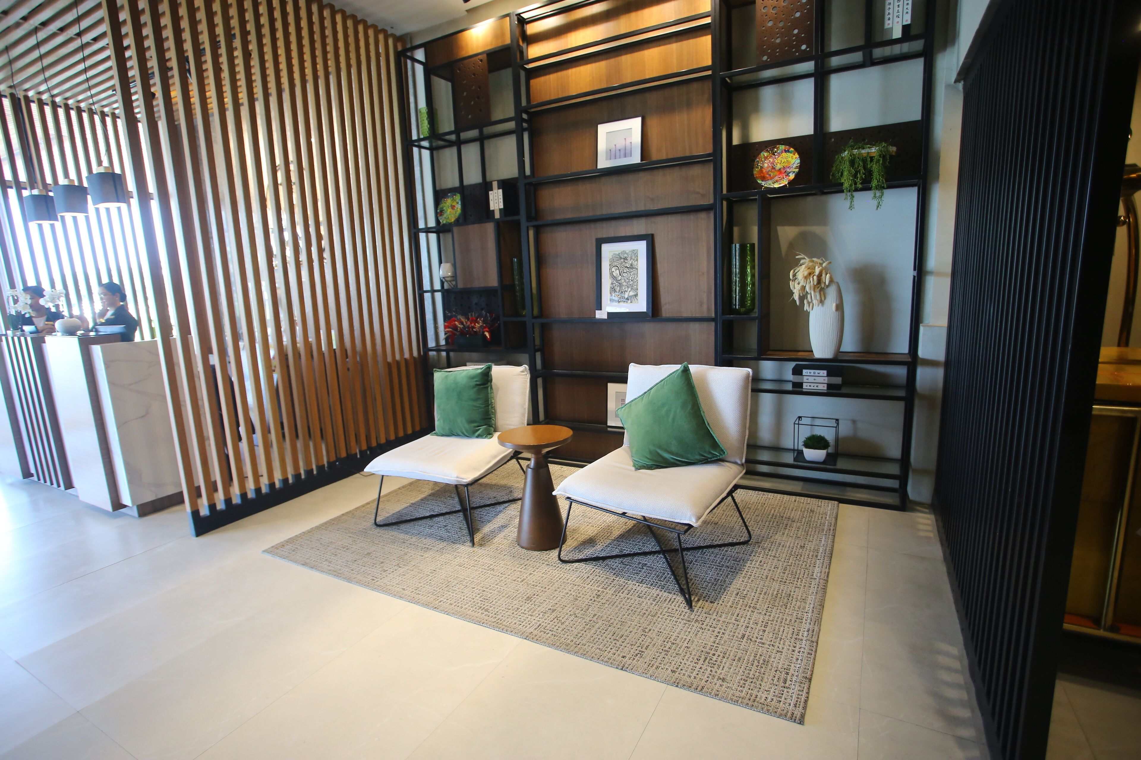 A modern lobby with two white cushioned chairs, a small round table, and a decorative wall with shelves.