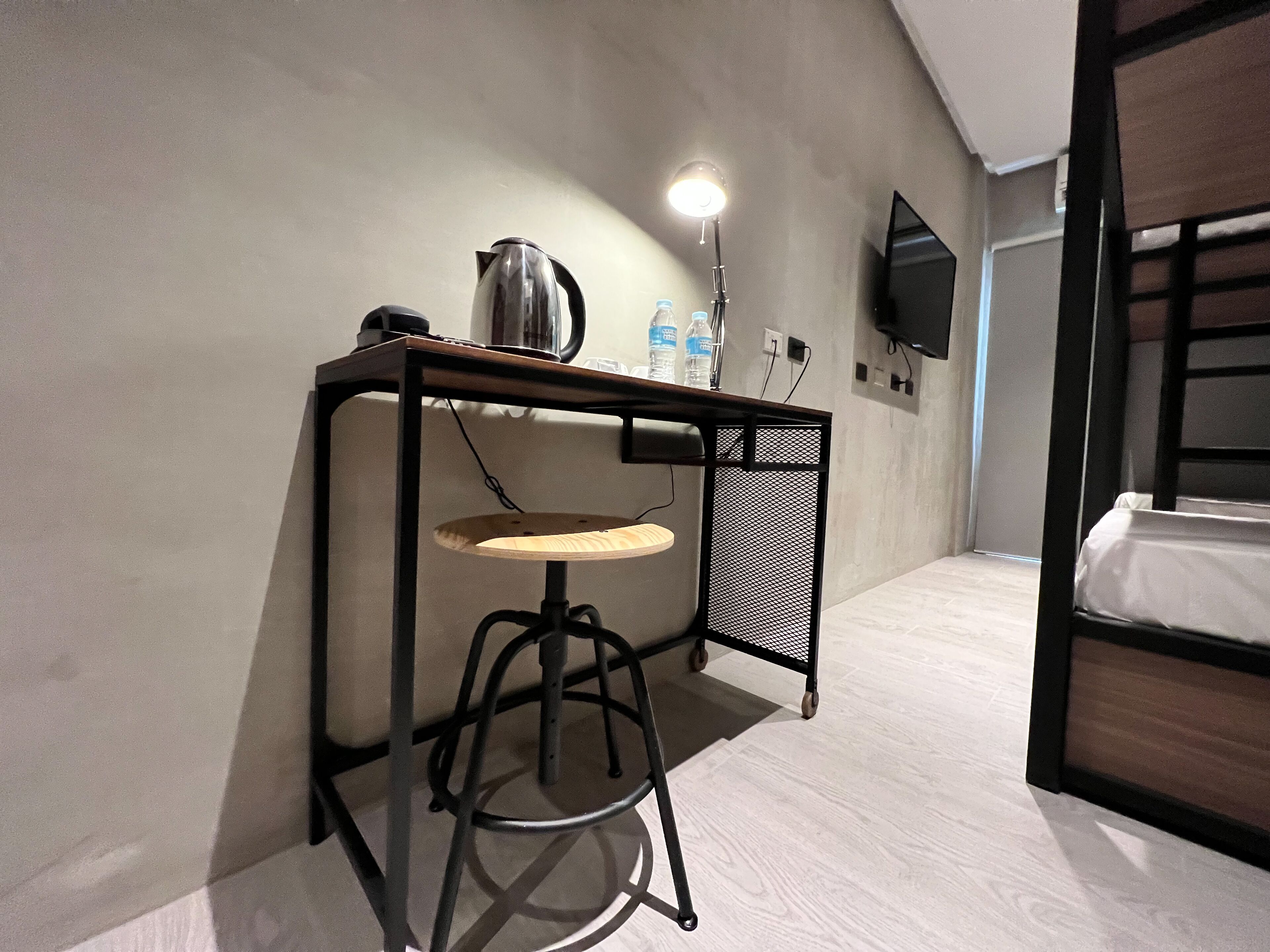 Camera d'albergo compatta con un letto singolo, una scrivania con una sedia, un bollitore, una lampada e una TV a muro.