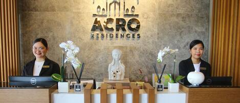 Una recepción con dos empleados, un mostrador de madera, una pared de mármol y el logotipo de "ACRO Residences".