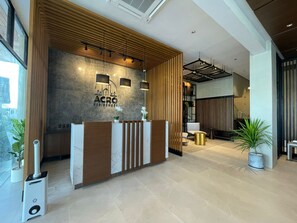 Welcome to our hotel, where a warm reception awaits with a beautifully designed lobby featuring a spacious reception desk, lush greenery, and a stunning staircase.