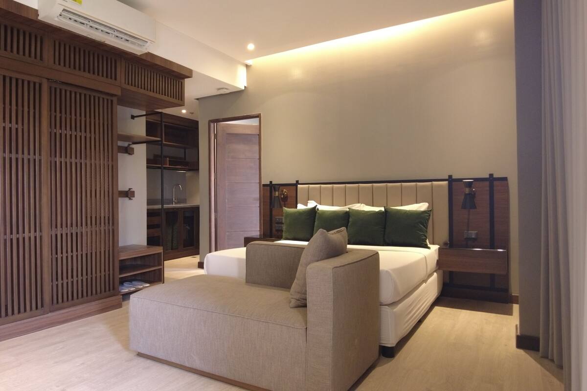 Een moderne slaapkamer met een bed, een slaapbank, een houten garderobe en een nachtkastje.