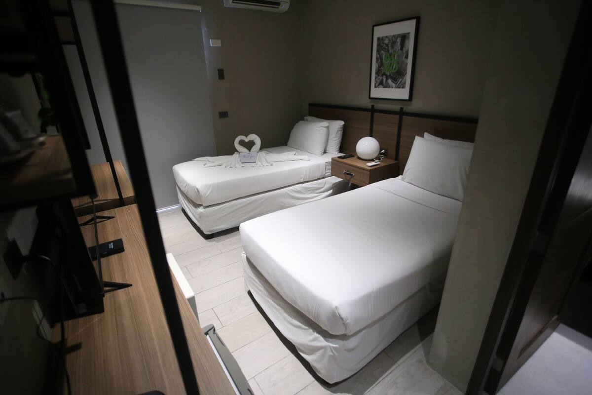 Een hotelkamer met twee eenpersoonsbedden, een nachtkastje met een lamp, een klein nachtkastje met een telefoon en afstandsbediening, en een lijstje op de muur.