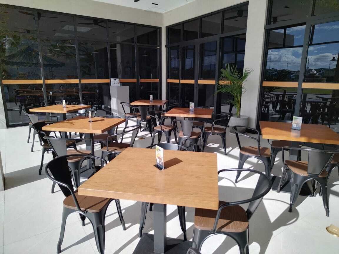 An outdoor cafe with multiple tables and chairs, large windows, and a view of the sky.