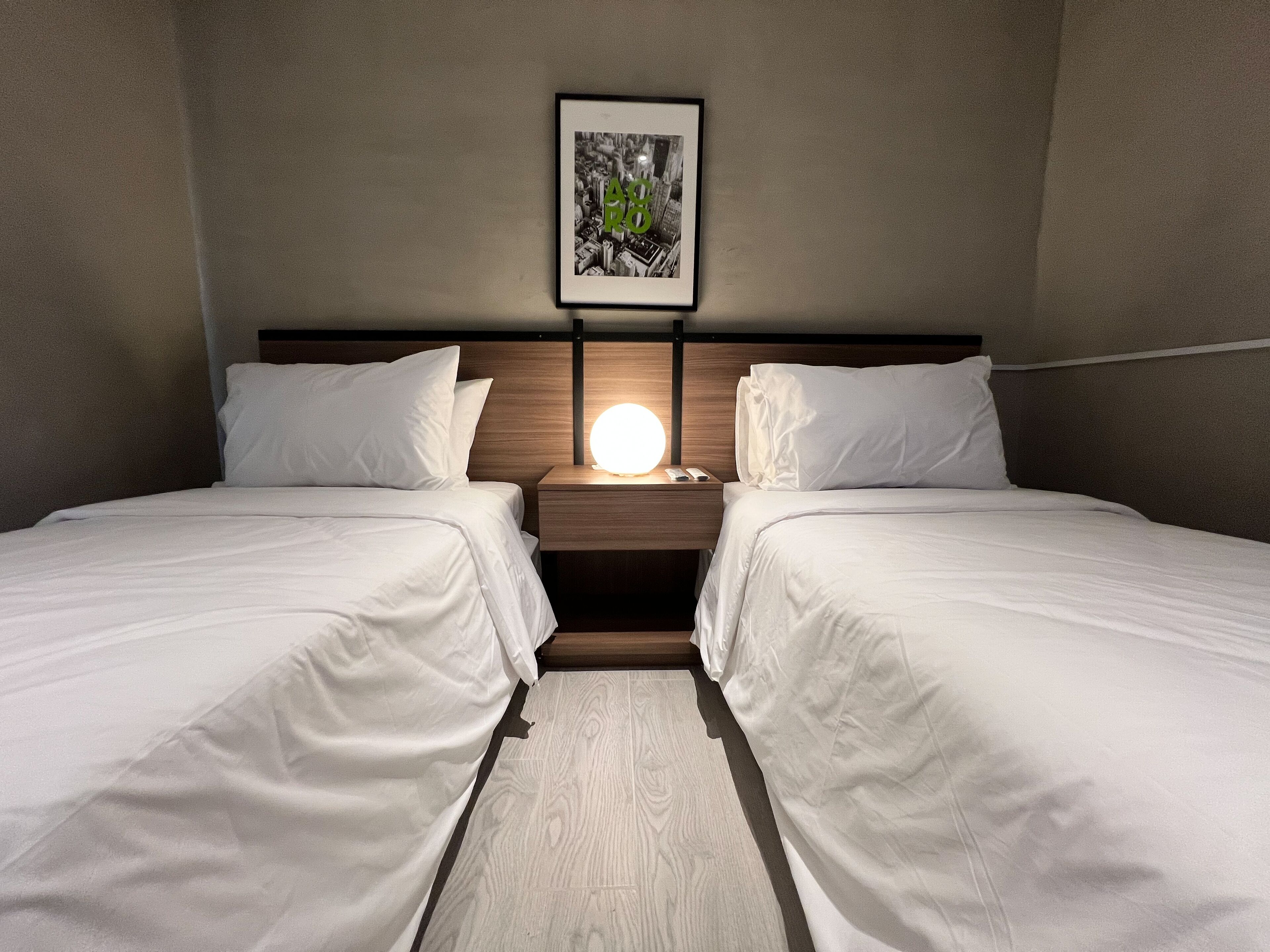 A hotel room with two beds, a nightstand with a lamp, and a framed picture on the wall.