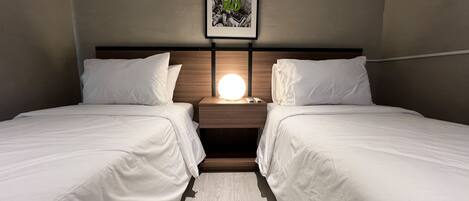 Habitación de hotel con dos camas, una mesita de noche con lámpara y un cuadro en la pared.