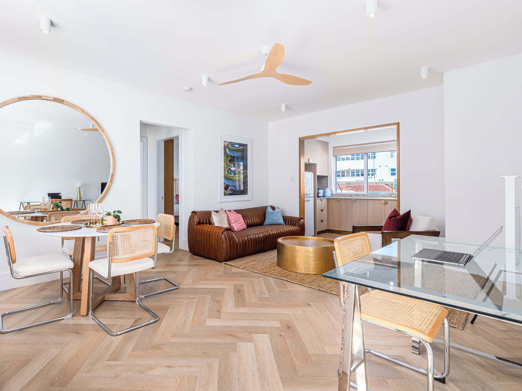 A modern living room with a dining area, a sofa, a glass table, and a ceiling fan.