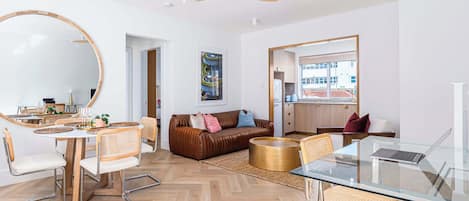A modern living room with a dining area, a sofa, a glass table, and a ceiling fan.