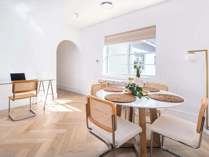 Zona pranzo moderna con un tavolo rotondo, sedie in vimini e un portatile su una scrivania.