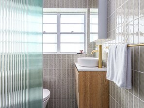 Un bagno con il water, un lavandino con rubinetto dorato, una finestra e un portasciugamani.