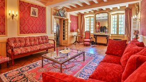 A room with a red patterned sofa, a glass coffee table, and a red armchair. There is a mirror on the wall and a door leading to another room. - Château de Taradel (Taradeau)