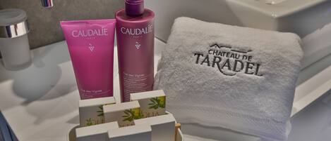A bathroom with a white sink, a mirror, and a towel with "CHATEAU DE TARADEL" text. There are two pink bottles labeled "CAUDALIE PARIS" and a white box with "VANITY KIT" text.
