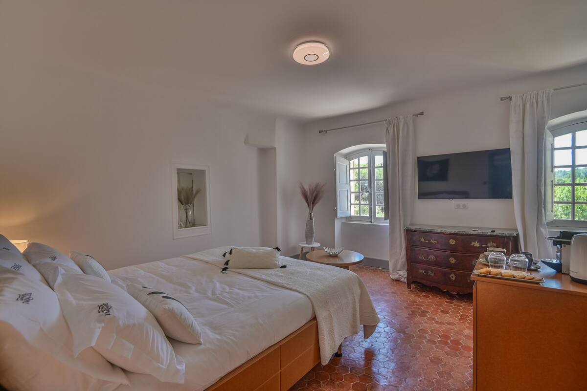 A bedroom with a bed, a dresser, a TV, and a window.