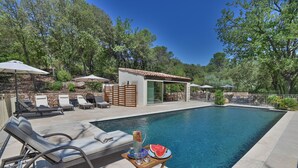 A swimming pool with lounge chairs and umbrellas, surrounded by trees and a small building. - Château de Taradel (Taradeau)