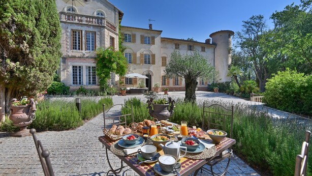 A table set with breakfast items in a courtyard with a building in the background. - Château de Taradel (Taradeau)