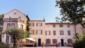 A historic building with a courtyard, featuring a central entrance, multiple windows with shutters, and surrounding greenery. - Château de Taradel (Taradeau)