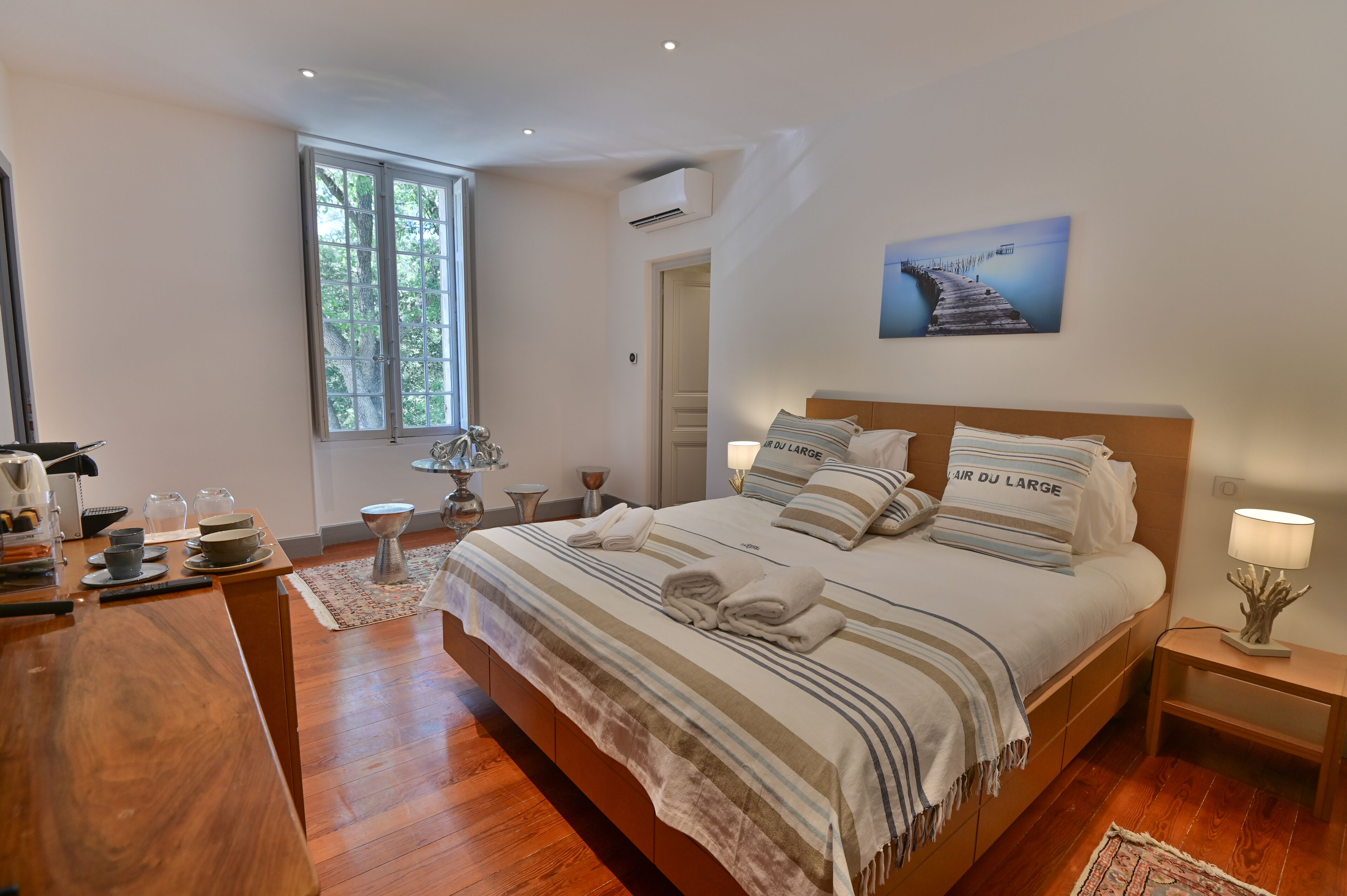 A bedroom with a large bed, a desk, a chair, a window, and a painting on the wall.
