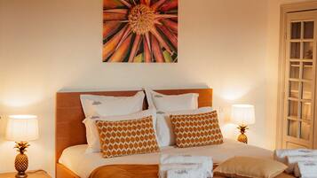 A hotel room with a bed, two bedside tables with lamps, a pineapple on one table, and a large floral artwork on the wall.