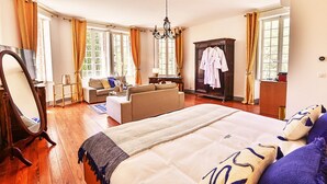 A bedroom with a large bed, a sitting area with a sofa, a wardrobe, and a mirror. - Château de Taradel (Taradeau)