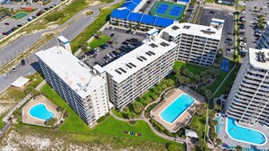 A multi-story hotel with a rooftop pool, a tennis court, and a parking lot.