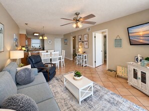 A living room with a sofa, coffee table, and a dining area with chairs. - Seaside Orange Beach, Indoor Pool, Tennis Courts! (Orange Beach)