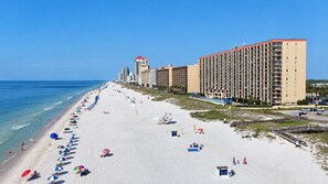 A beach with a row of beach umbrellas, a lifeguard tower, and a large hotel building with multiple floors.