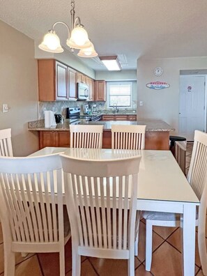 A kitchen with wooden cabinets, a white countertop, and a dining area with a white table and chairs.