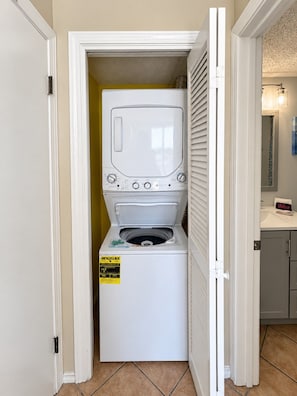 A compact laundry room with a front-loading washer and dryer, a door, and a small countertop with a makeup item.