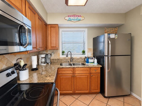 A kitchen with wooden cabinets, a stainless steel refrigerator, a microwave, and a stove.