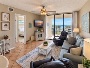 A living room with a sofa, armchairs, a coffee table, and a TV. There is a balcony with a view of the ocean. - Seaside Orange Beach, Indoor Pool, Tennis Courts! (Orange Beach)
