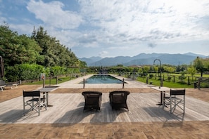 Zona de piscina con vistas a montañas, rodeada de vegetación y amueblada con asientos de exterior.