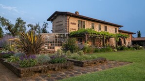 Un grand bâtiment de style rustique, doté d’une façade en briques, d’une véranda en verre et d’un jardin bien entretenu avec diverses plantes et une pelouse.
