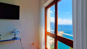 A room with a large window overlooking a coastal view, a lamp on a shelf, and a power outlet.