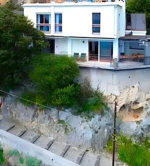 Un immeuble à plusieurs étages doté de balcons, d’un mur de soutènement en pierre et de végétation.