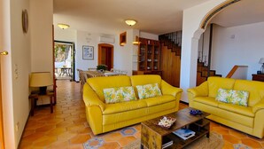 A living room with two yellow sofas, a wooden coffee table, and a staircase leading to another level.
