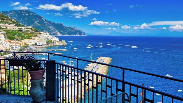 A coastal town with a marina, boats, and a mountainous backdrop.