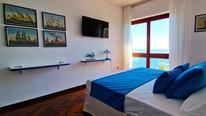 A bedroom with a bed, a TV, artwork, and a window with a view.