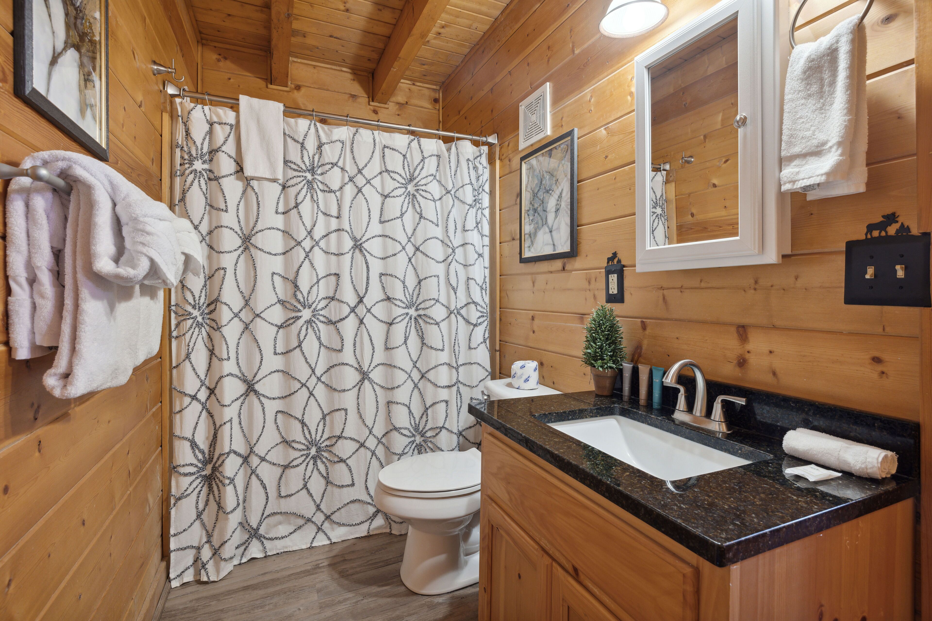 A wooden cabin bathroom with a shower curtain, toilet, sink, and towels.