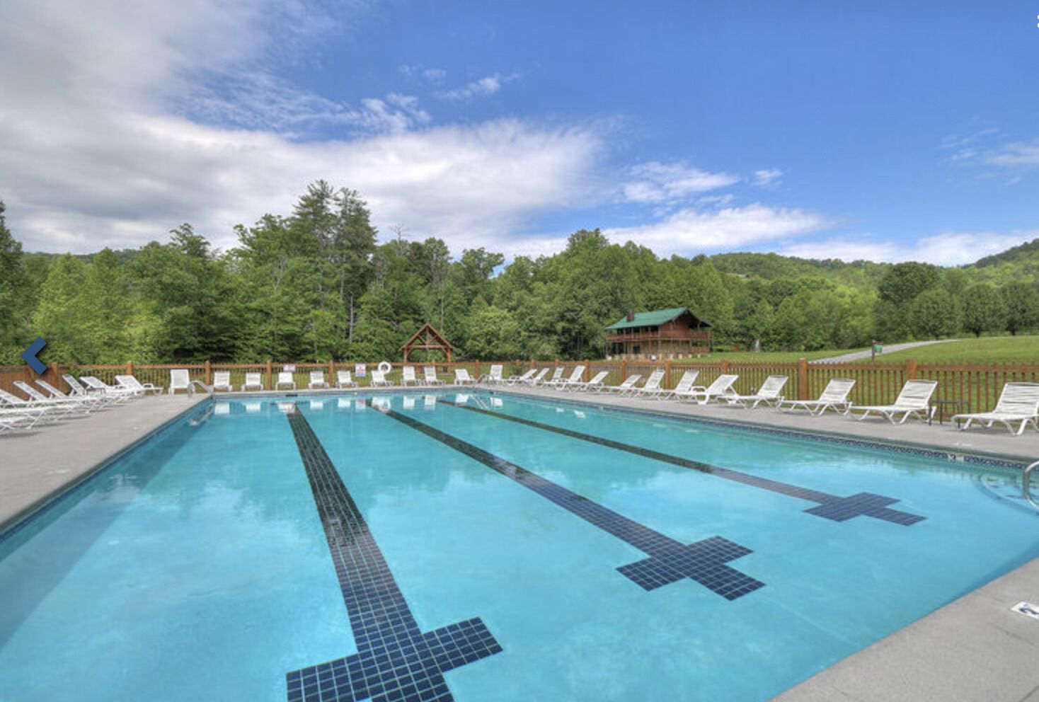 A rectangular swimming pool with lane dividers, surrounded by white lounge chairs and a wooden fence.