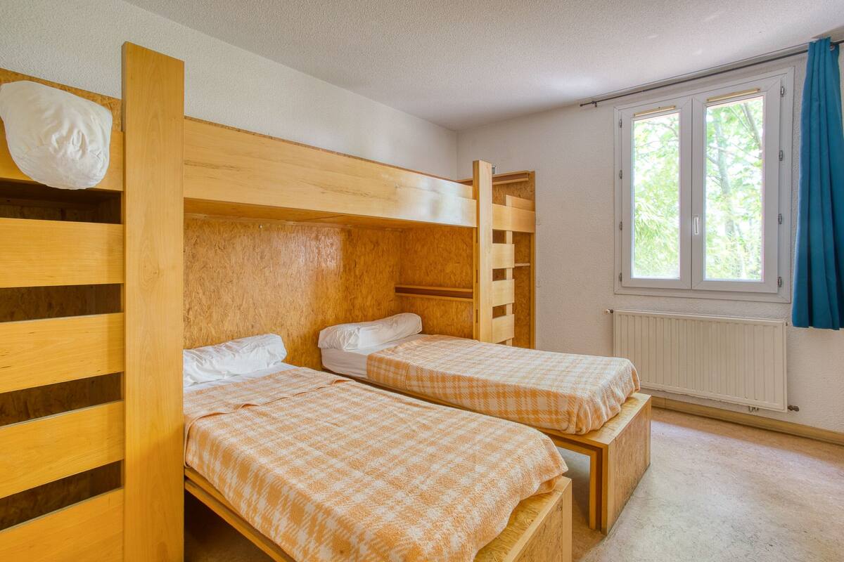 Una habitación con dos literas de madera, una ventana con cortinas y un radiador.