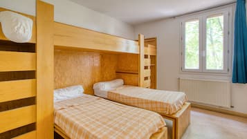 A room with two wooden bunk beds, a window with curtains, and a radiator.
